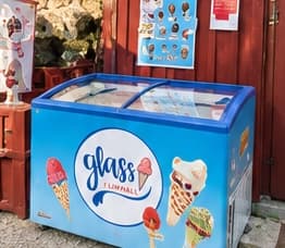 The blue ice cream freezer with the Glass i Limhall logo in front of the shed