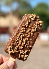 An ice cream bar coated in chocolate and chopped nuts
